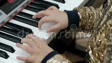 一个穿着闪闪发光的金色衬衫的女孩弹钢琴。 儿童手指按电子合成器的白键